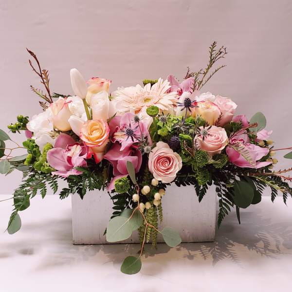 Low pastel arrangement of roses, orchids, and mixed blooms in a white wooden box.