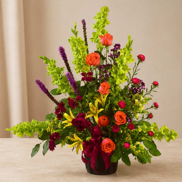 Colorful floral arrangement with orange roses, yellow lilies, and purple spikes in a vase