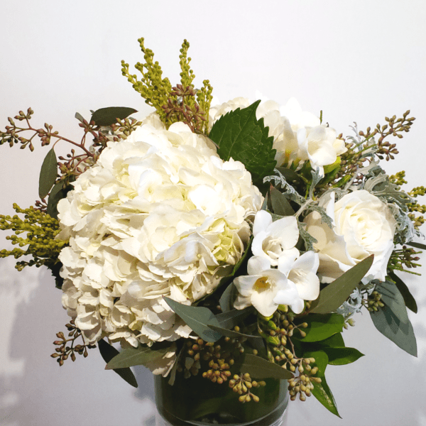 White hydrangeas and roses in a glass vase with mixed greenery