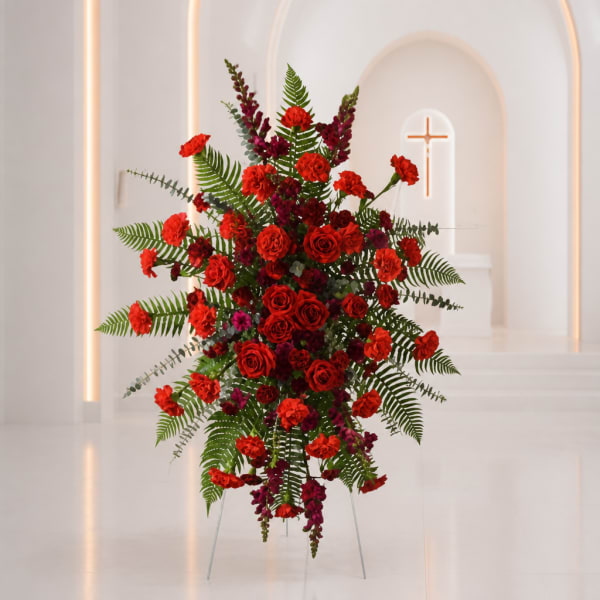 Tall red floral spray on a stand with fern foliage in a white chapel setting