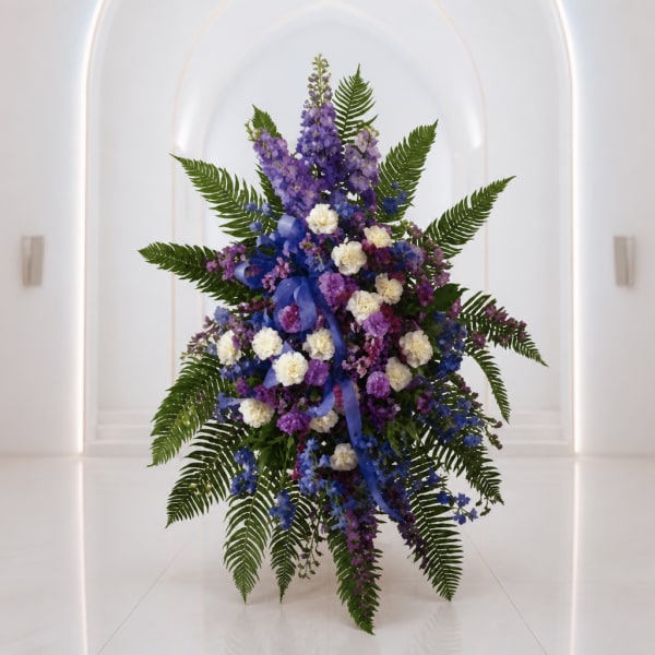Tall purple and white floral arrangement with fern fronds and blue ribbon