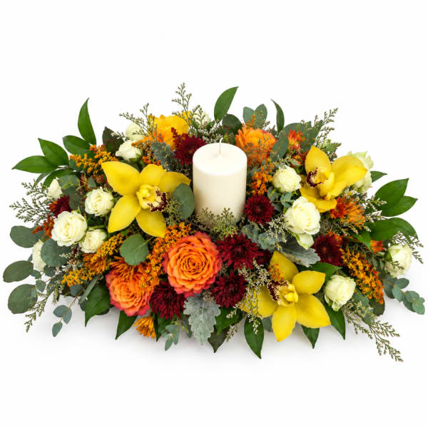 Yellow orchids and roses arranged around a white pillar candle