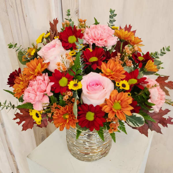 Mixed bouquet of pink, red, orange, and yellow flowers in a silver vase