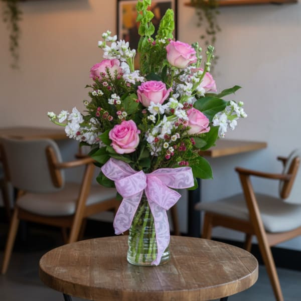 Pink roses and white filler flowers in a glass vase with a pink ribbon