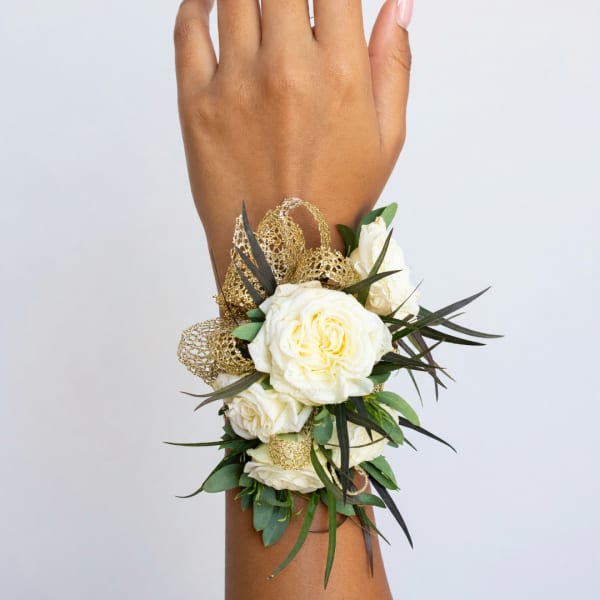 White rose wrist corsage with gold ribbon and greenery on a wrist