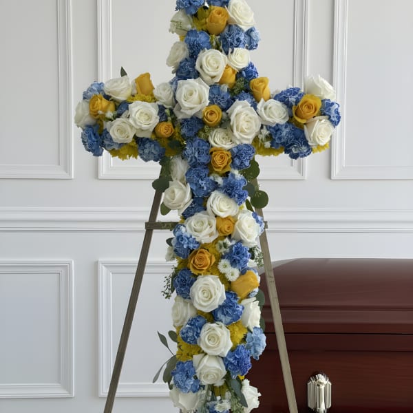 Cross-shaped floral tribute with white, blue, and yellow roses on an easel