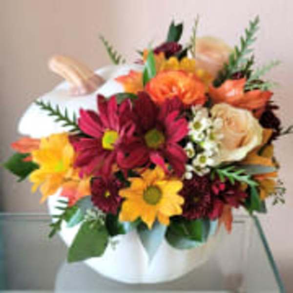 Mixed bouquet of orange, yellow, and burgundy flowers in a white vase