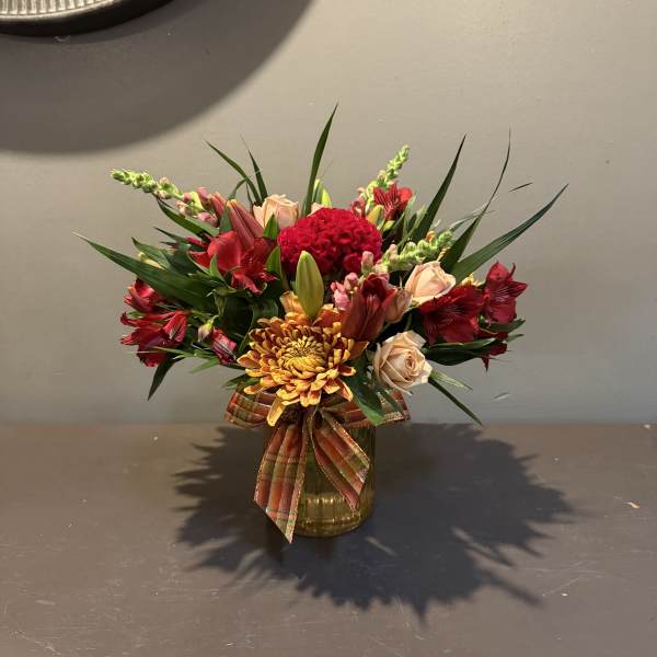 Mixed bouquet of red, peach, and yellow flowers in a glass vase with a plaid ribbon