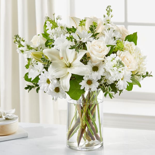 White roses, lilies, and daisies arranged in a clear glass vase