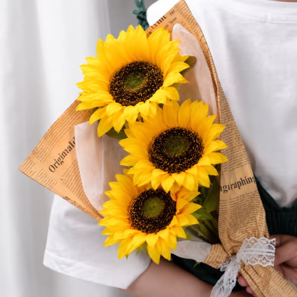 Three sunflowers wrapped in newspaper-style paper with a lace ribbon