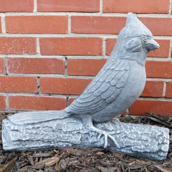 Gray bird statue perched on a faux log against a brick wall