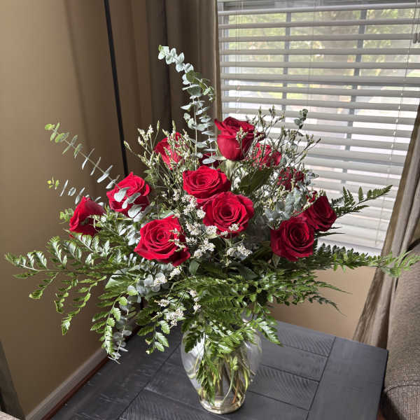 Red roses arranged in a clear glass vase with airy greenery