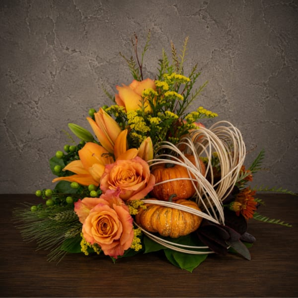 Orange roses and lilies arranged with pumpkins and wicker loops