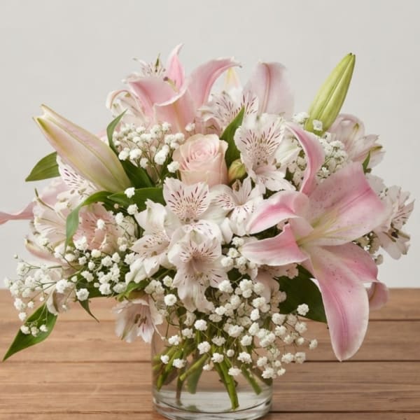 Pink lilies and white filler flowers arranged in a clear glass vase