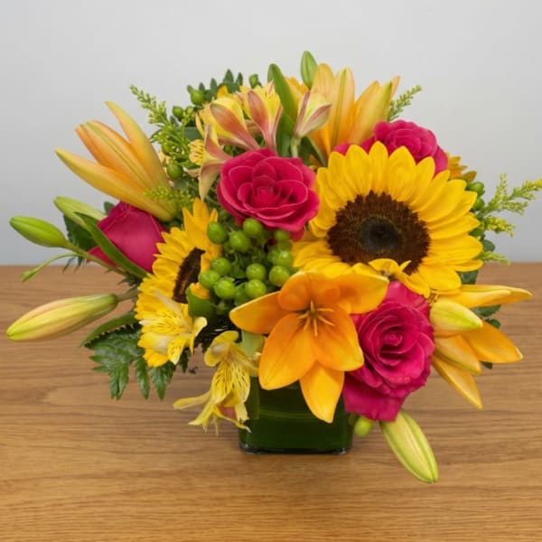 Bright mixed bouquet with sunflowers, pink roses, and orange lilies in a glass vase