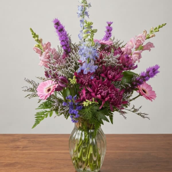 Mixed pink, purple, and blue flowers in a clear glass vase