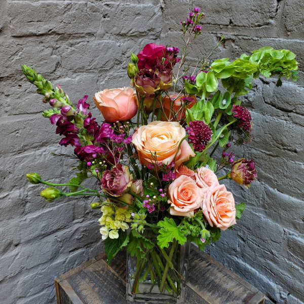 Mixed bouquet of peach roses and purple flowers in a clear glass vase