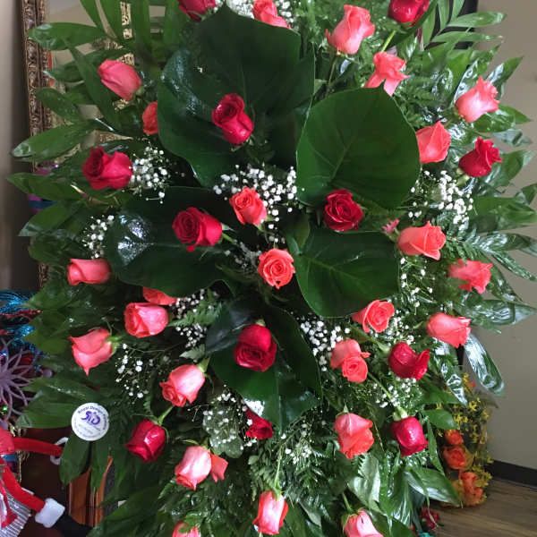 Large standing arrangement of red and pink roses with glossy greenery