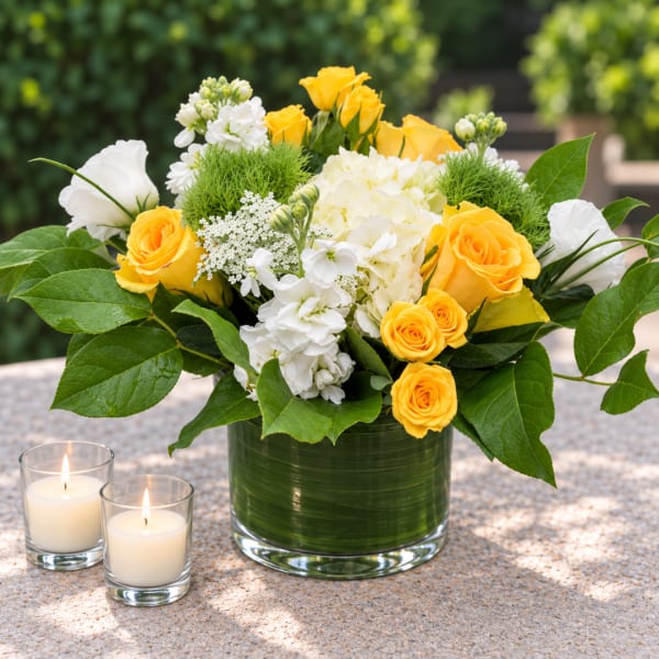 Yellow and white rose arrangement in a glass vase with two lit candles
