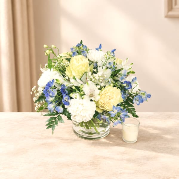 Blue and white flower arrangement in a clear glass bowl with a small candle beside it