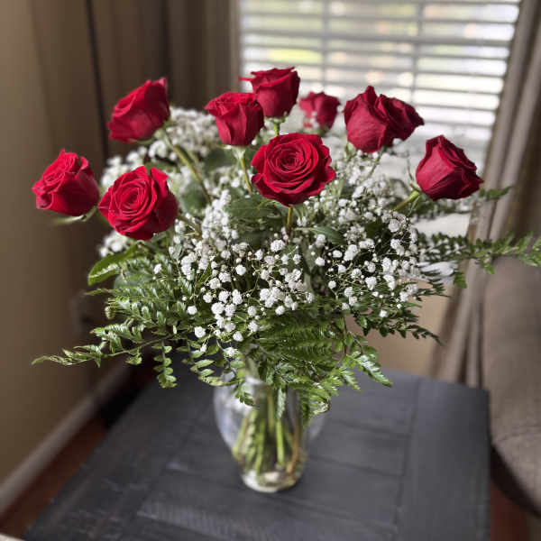 Red roses arranged in a clear glass vase with white baby's breath