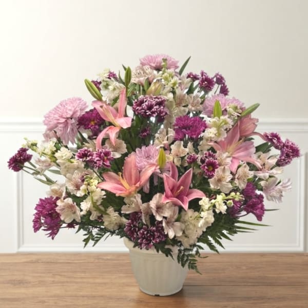 Pink lilies and purple mixed flowers arranged in a white vase
