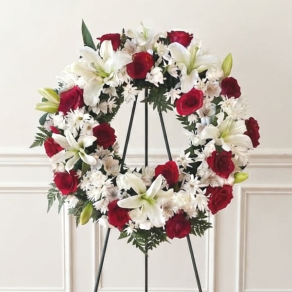 Red roses and white lilies arranged in a wreath on a black stand
