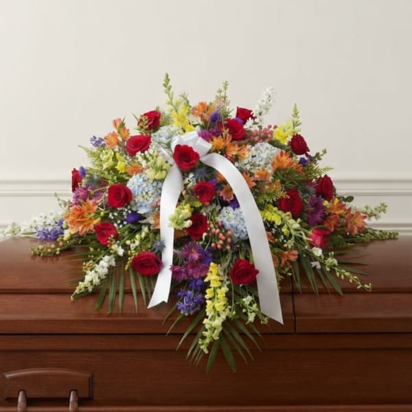 Colorful floral casket spray with red roses and a white ribbon