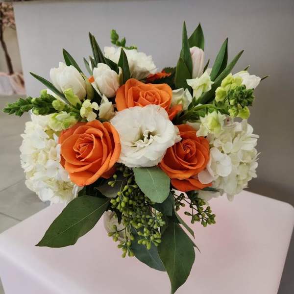 Compact bouquet of orange roses and white blooms in a clear glass vase
