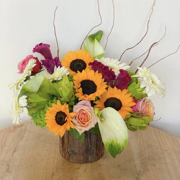 Mixed bouquet with sunflowers, roses, white daisies, and green calla lilies in a wood container