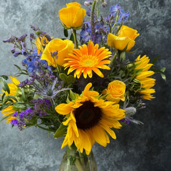 Bouquet of yellow roses, sunflowers, and purple flowers in a glass vase