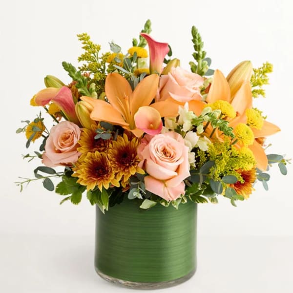 Mixed bouquet of peach lilies, pink roses, and yellow flowers in a green vase