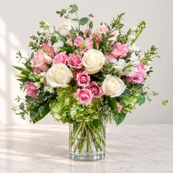 Pink and white roses with mixed blooms in a clear glass vase