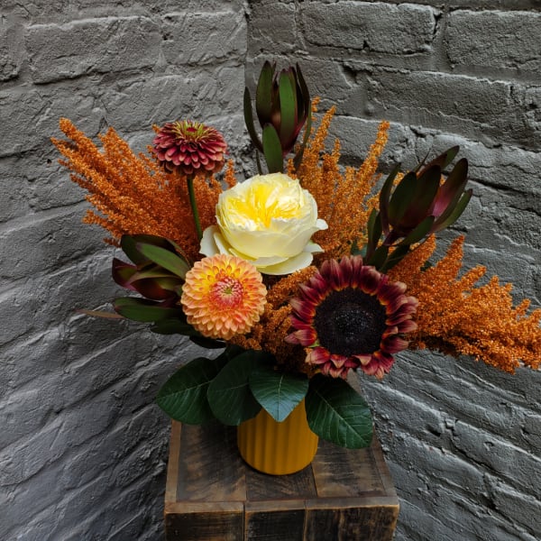 Mixed floral arrangement in a yellow vase with orange accents