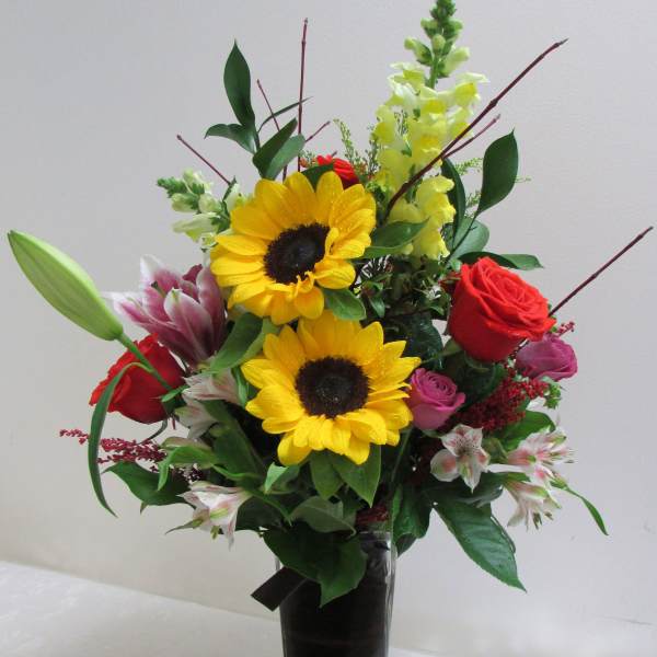 Mixed bouquet with sunflowers, roses, lilies, and snapdragons in a tall vase
