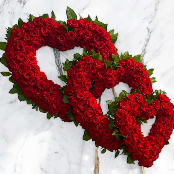 Three red rose heart wreaths on sticks against a white marble background