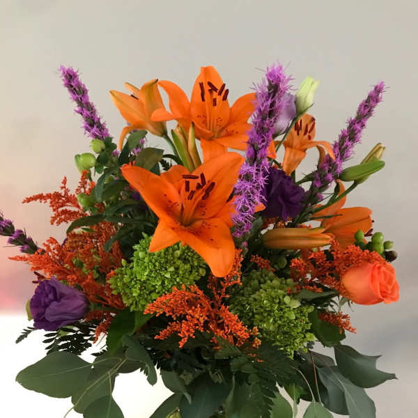 Orange lilies and purple flowers in a glass vase