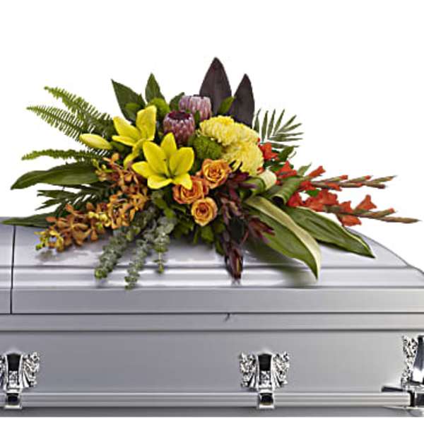 Floral spray on a silver casket with yellow lilies and orange roses