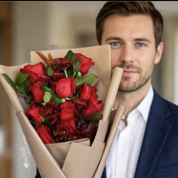Man holding a bouquet of red roses wrapped in tan paper