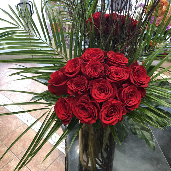 Red roses arranged in a tall glass vase with palm fronds