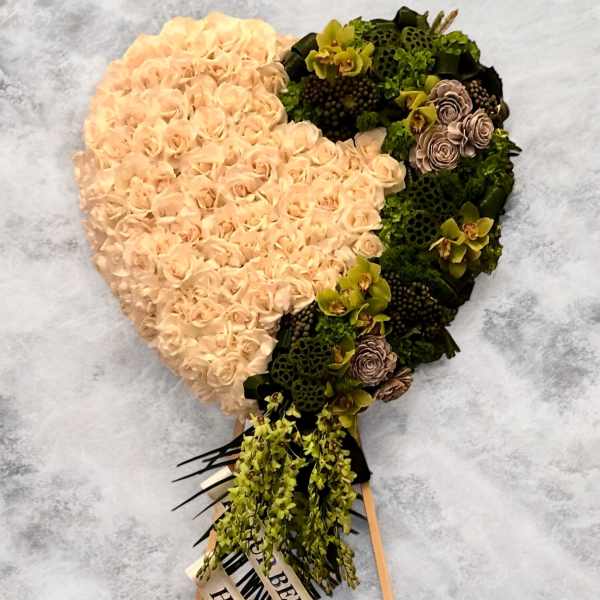 Heart-shaped floral arrangement with pale peach roses and green accents on a stand