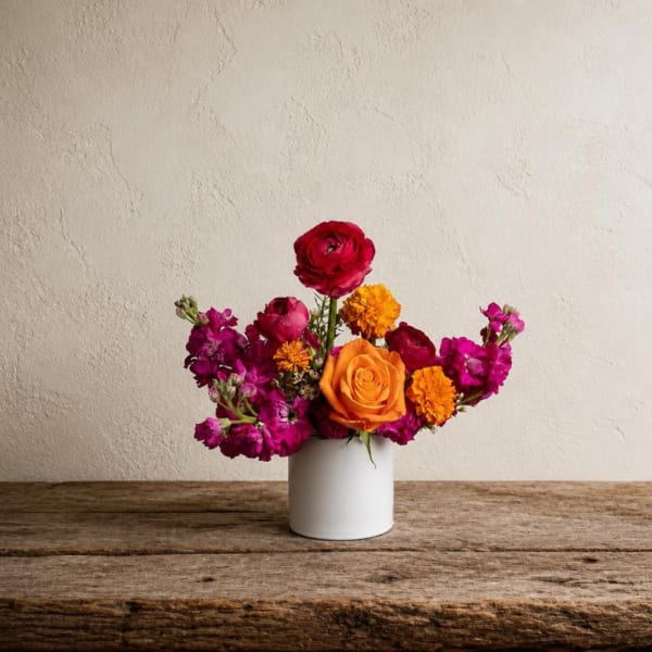 Colorful mixed flower arrangement in a white vase on a wooden table