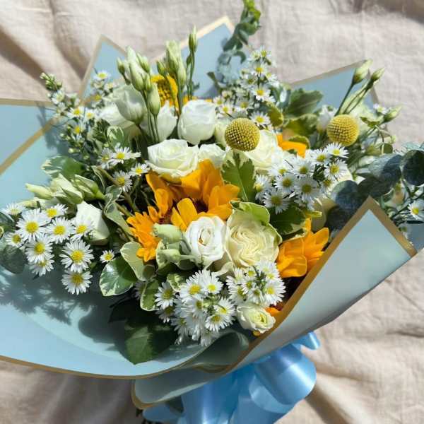 Bouquet of white and yellow flowers wrapped in pale blue paper with a blue ribbon