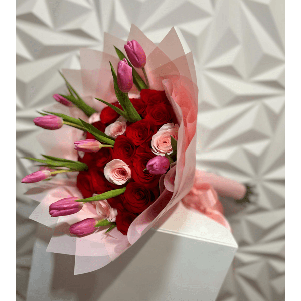 Bouquet of red roses and pink tulips wrapped in pale pink paper