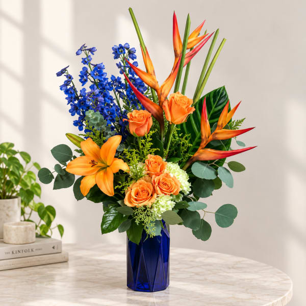 Orange roses, lilies, and blue delphinium in a cobalt vase