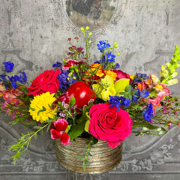 Colorful mixed flower arrangement in a gold round vase with a red ornament