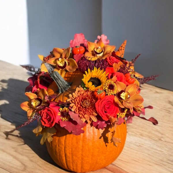 Fall floral arrangement in a pumpkin container with sunflowers and roses