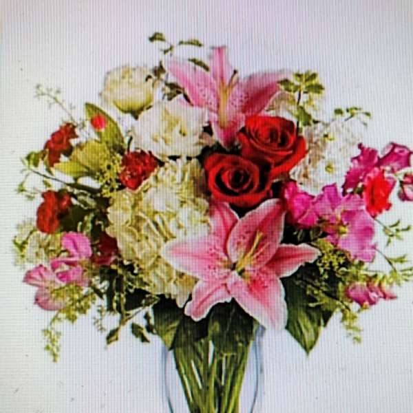 Mixed bouquet of pink lilies, red roses, and white flowers in a clear vase