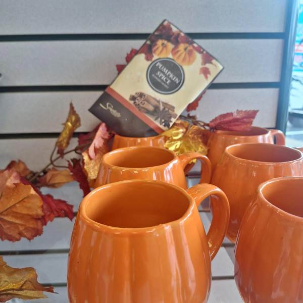 Orange pumpkin-shaped mugs displayed with autumn leaf decor