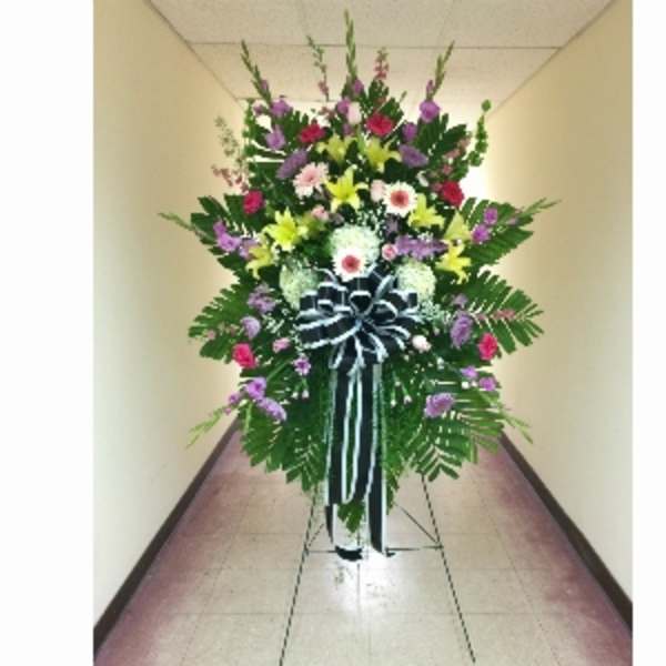 Tall standing spray of mixed colorful flowers with a large black and white bow on an easel.